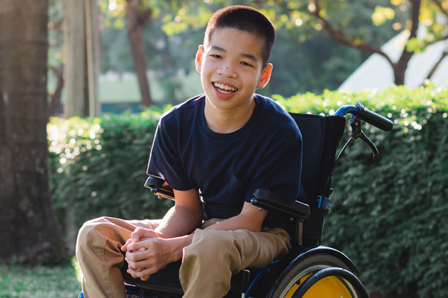 Stock image of a boy smiling while sitting in a mobility device.