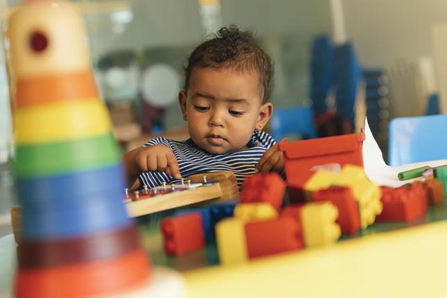 A toddler plays with toys in a classroom-type setting.