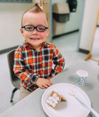 A young boy with Sturge-Weber syndrome sits at a table and smiles.