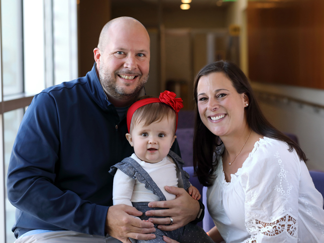 A baby girl sits with her parents.