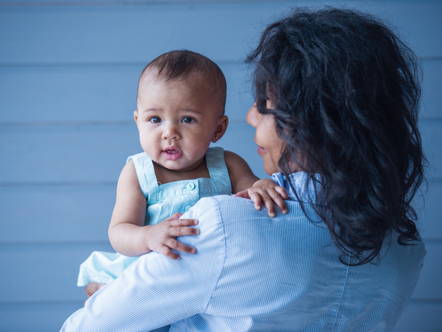 A little baby girl in her mom's arms, against a gray background