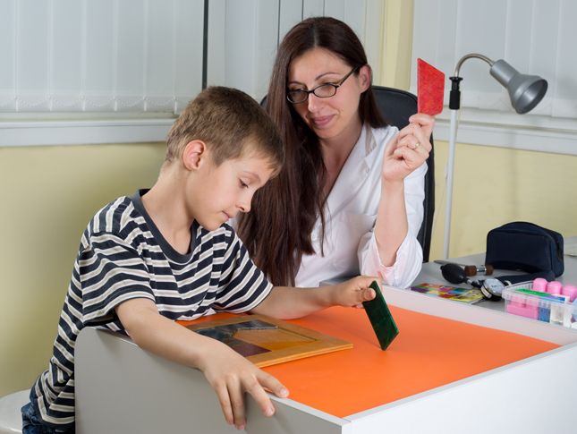 A child puts together a puzzle of shapes with help from an adult.