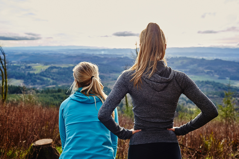 Two women with their backs to the camera look out over a mountain