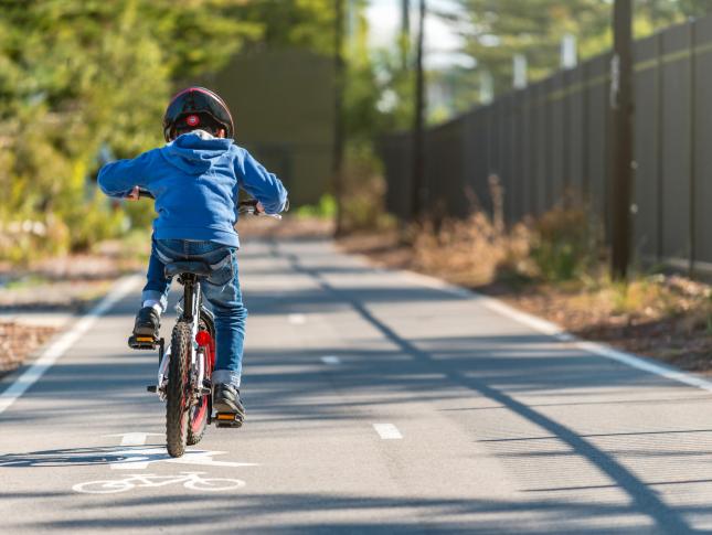 A photograph of a boy riding a bike along a sidewalk