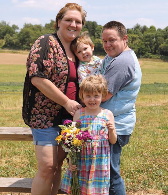 A family portrait of two women and their son and daughter, a little girl and a little boy, in a rural setting.