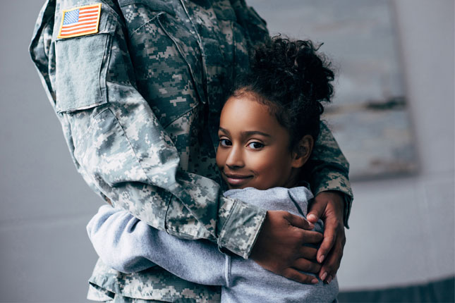 A little girl smiles while hugging a soldier.