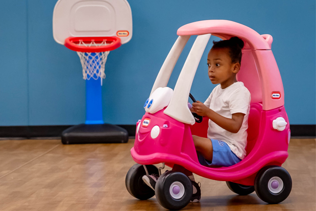 A little girl rides a pink cozy coupe.