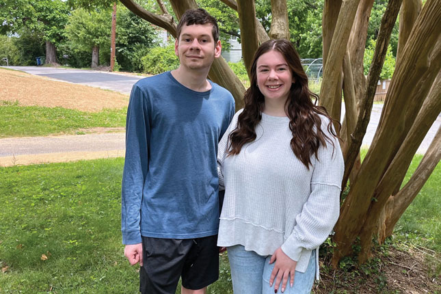 Alyssa and Michael smile while standing in front of a tree.