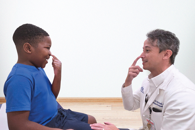 Dr. Eric Mallack and a Kennedy Krieger patient smile as they both touch their noses.