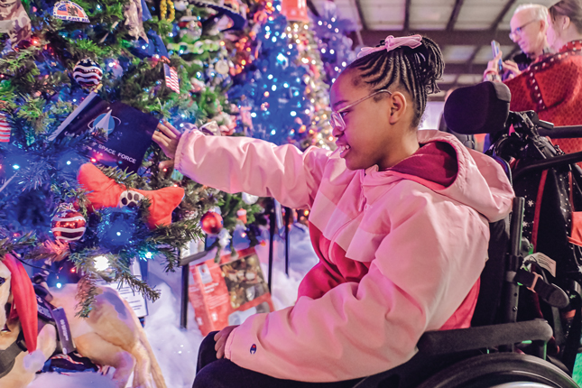 A little girl smiles while looking at a grove of lighted trees.