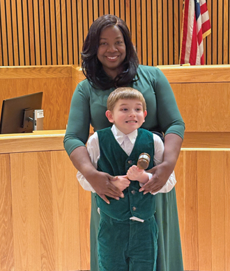 A Therapeutic Foster Care parent and her foster son smile while standing inside of a court room.