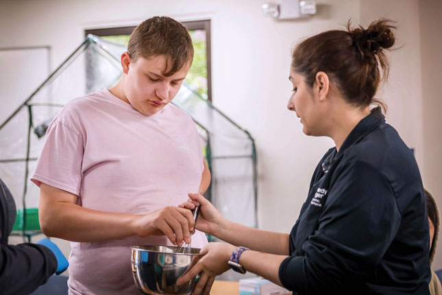 A student stirs a bowl while working with a teacher during a life skills class.