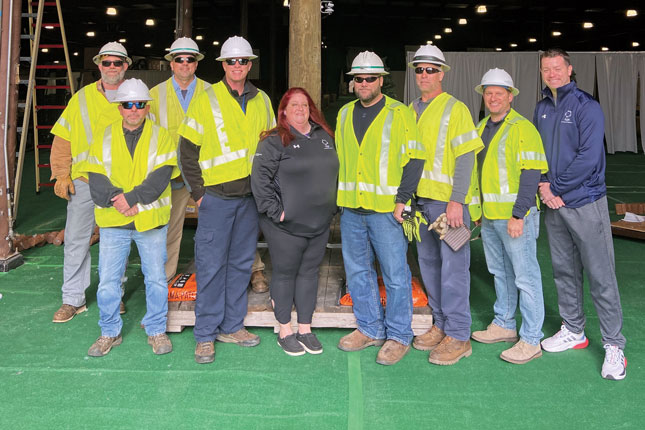 A group of nine people, mostly men and mostly wearing bright yellow construction vests and helmets, pose for the camera.
