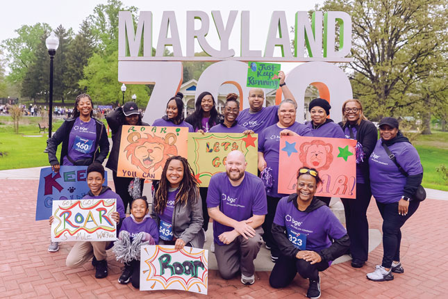 A group of people in purple shirts that say “BGE” pose in front of a sign that says “Maryland Zoo.”