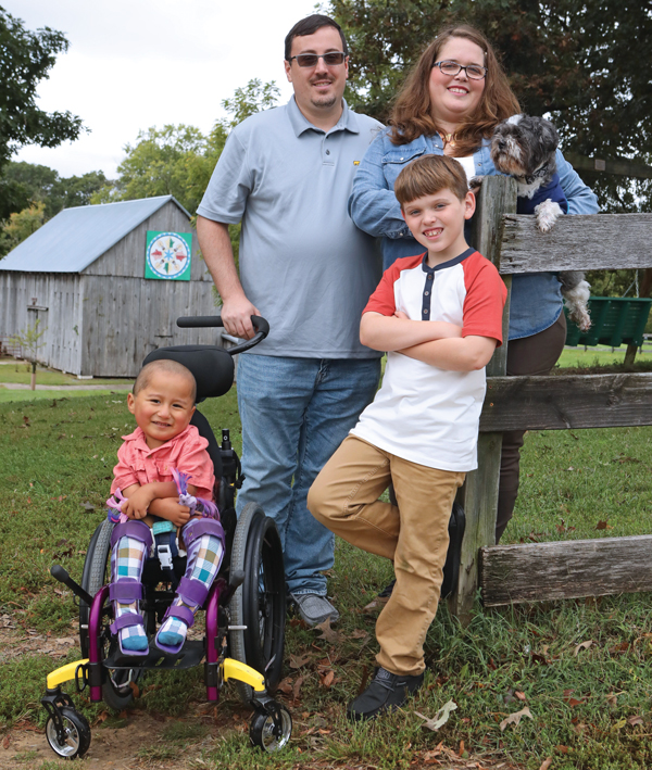 Posed family photo of a mom and dad and their two young sons and small dog. The younger son sits in a wheelchair.)