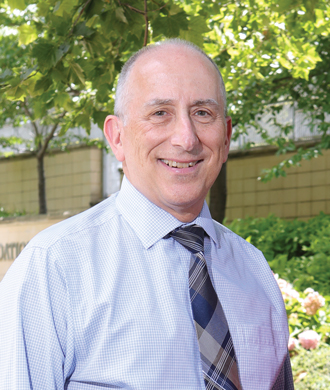 Posed outdoor photo of a smiling man in business attire.)