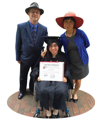Valerie, smiling and wearing a graduation cap and gown, sits in a wheelchair, holding a diploma. Behind her stand her parents, who are also smiling.