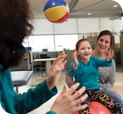 Physical therapist Lizzie Neighbors (right) helps Caetlyn balance on a therapy ball while Caryn and Caetlyn toss a beach ball back and forth during physical therapy.