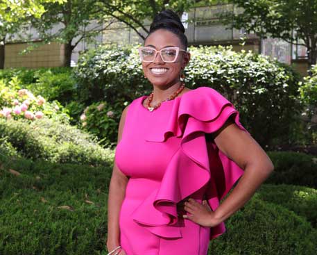 A young woman stands outside. She is smiling and appears confident.