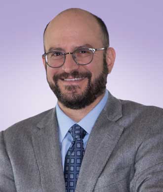 A posed headshot photo of Dr. Bradley Schlaggar. He is smiling and is wearing glasses and a suit and tie.