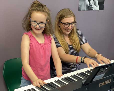 A young girl and a woman play an electric keyboard together. Both are smiling.