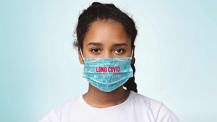 A young girl wears a facemask that says LONG COVID.
