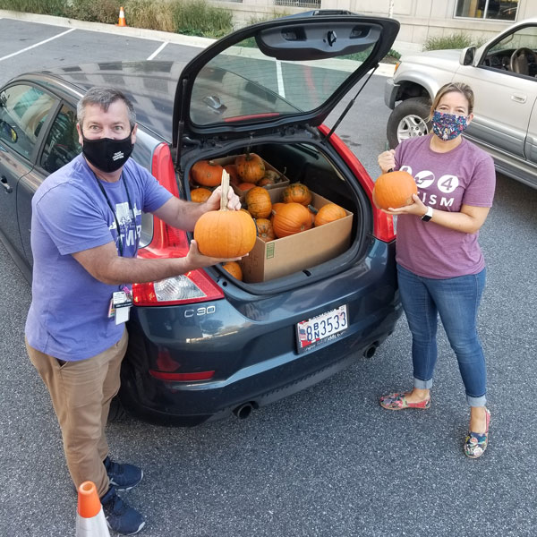 Two Kennedy Krieger load small pumpkins into the back of a car.