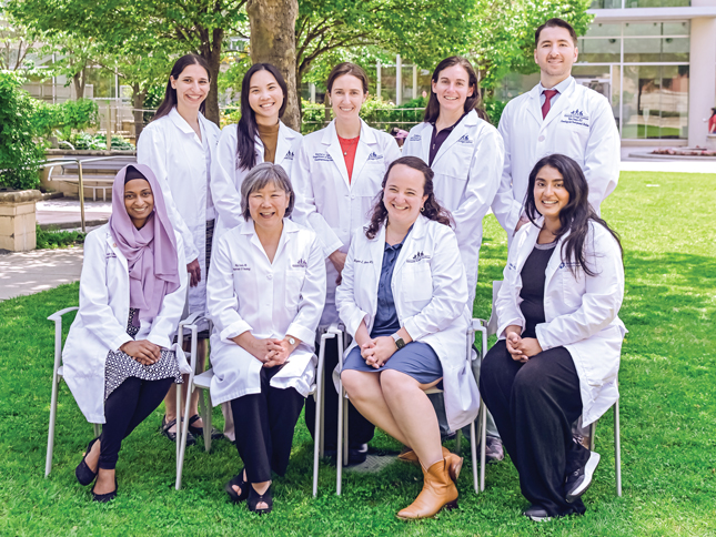 A group of Kennedy Krieger doctors wearing white coats smile while posing for a group photo in Kennedy Krieger's therapy garden.