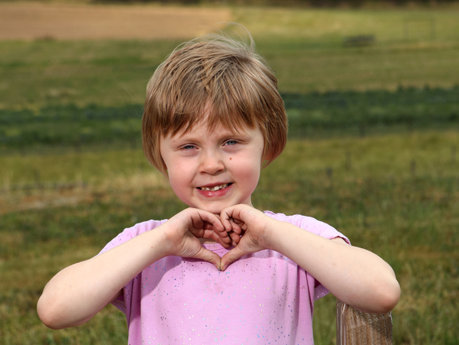 A young girl smiles while holding her hands in the shape of a heart.