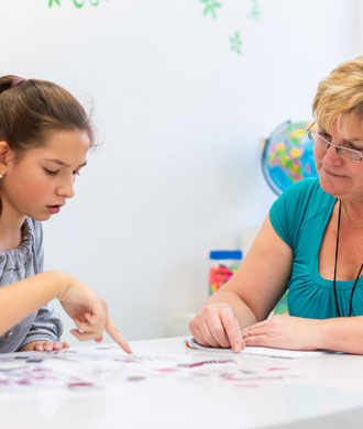 A female therapist sits at a table with a teenage girl while reviewing a test.