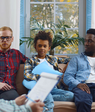 A male gay couple and their foster son speak with a social worker at home.