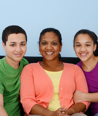 A mother and two children, son and daughter, sitting on a sofa together smiling.