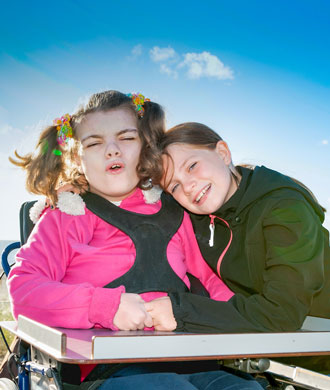 A child embraces her sister, whose sitting in a wheelchair.