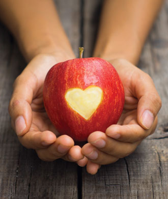 Two hands holding an red apple with a heart in the middle. 