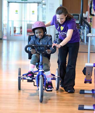 A physical therapist helps her patient, a young girl, to ride a book inside the therapy room.