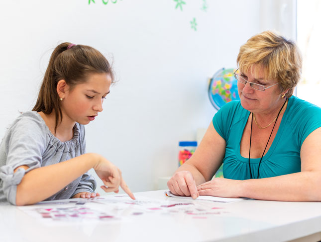 A female therapist sits at a table with a teenage girl while reviewing a test.