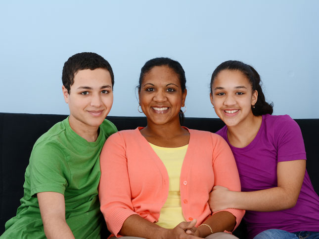 A mother and two children, son and daughter, sitting on a sofa together smiling.