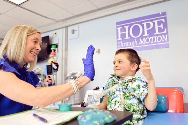 A patient of the Pediatric Rehabilitation Unit high fives an SLP.