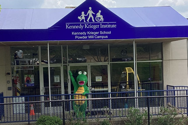 The Powder Mill Campus mascot, an alligator, stands under the awning of the school's main entrance.
