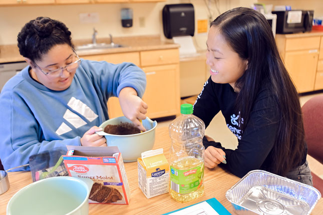 A patient stirs cake mix inside of a bowl with the help of a therapist.