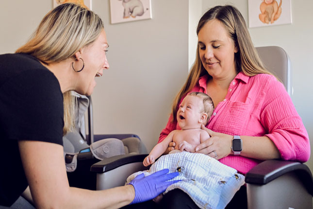 A baby smiles at a nurse while being held by its mother.