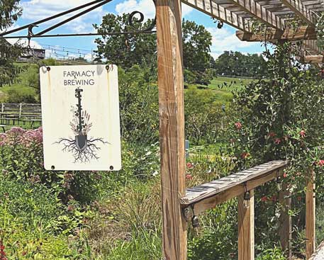 A Farmacy Brewing sign hangs outside on a wooden post. 