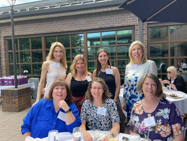 Seven women, three sitting and four standing, pose for a photo at the member luncheon. 