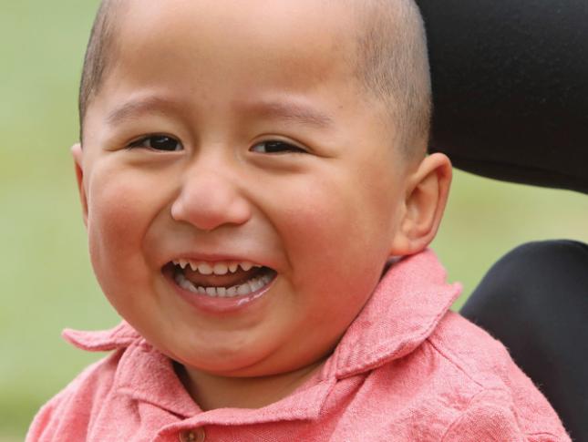 A young boy sitting in a wheelchair smiles.
