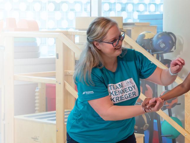 A young girl participates in physical therapy using assistive technology. Two female therapists are overseeing the session.