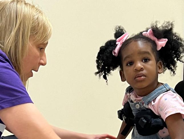A physical therapist assists a little girl who is using a mobility device.