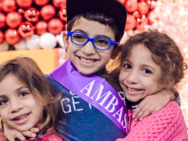 A Kennedy Krieger ambassador and his sisters smile at Festival of Trees.