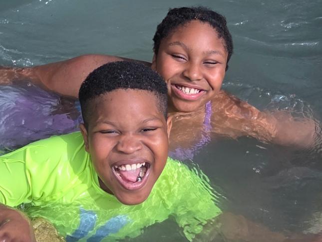 A Kennedy Krieger ambassador and his sister smile while swimming.