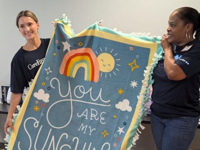 Two women wearing CareFirst shirts unfurl a blanket during a volunteer event.