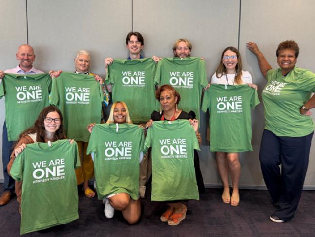 A group of Kennedy Krieger staff members either wearing or holding green We Are One Kennedy Krieger t-shirts.